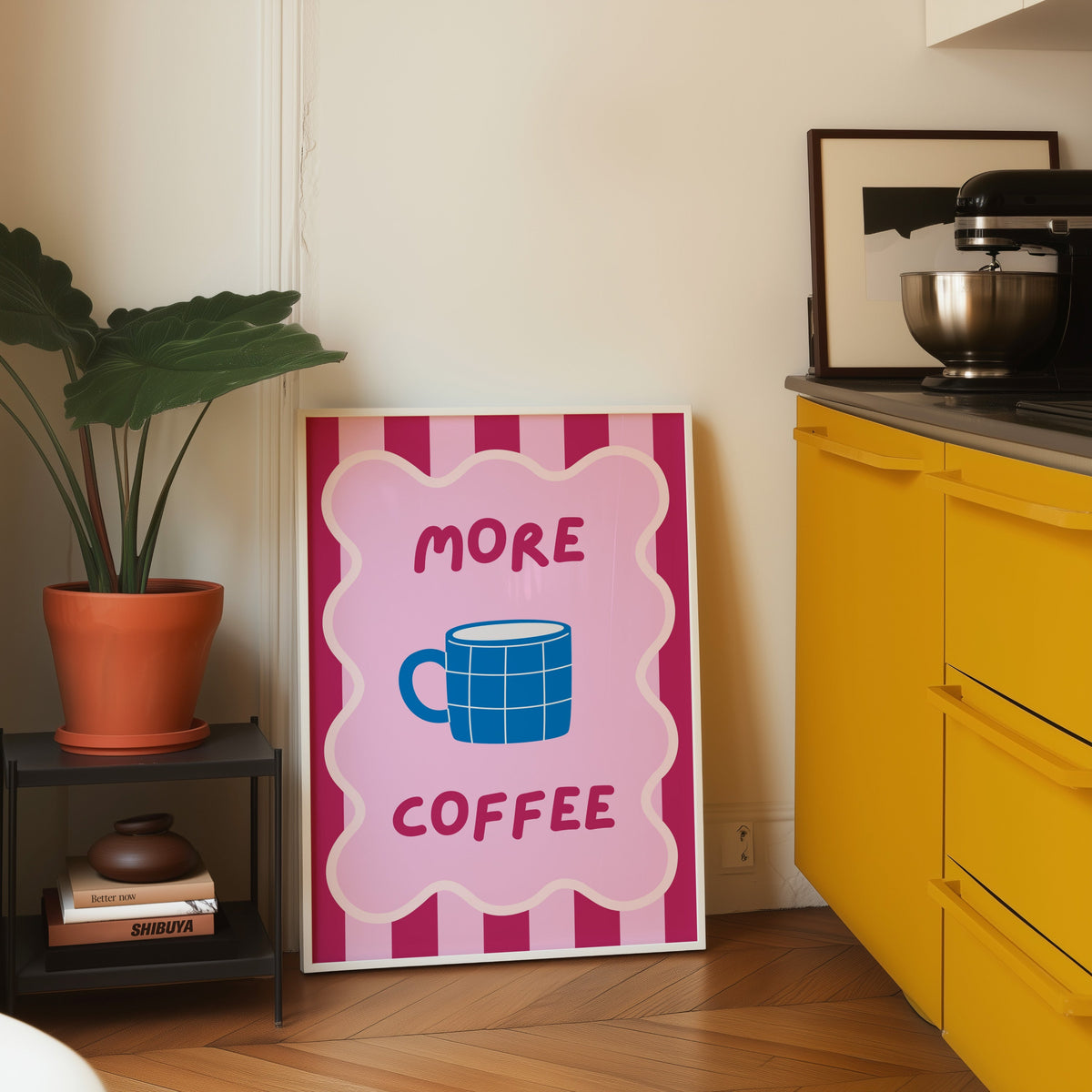 More Coffee mug print in a white frame leaning on parquet beside a bright yellow kitchen