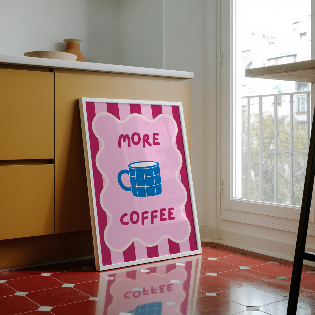 More Coffee mug print in a white frame against yellow cabinets on a red tiled floor