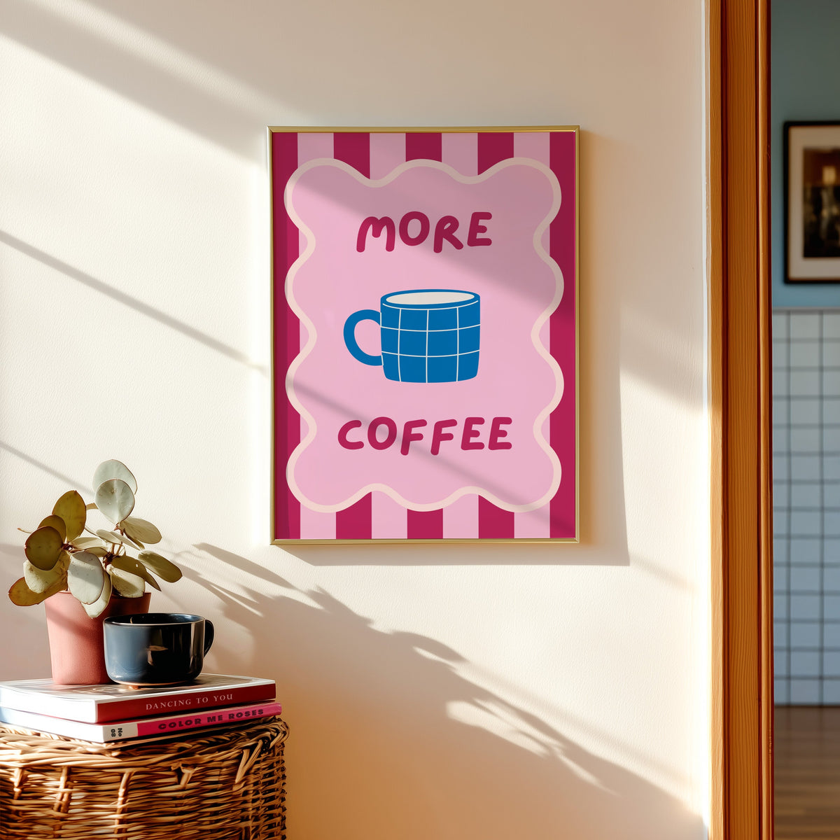 More Coffee mug print shown in a gold frame above a basket of books and a pilea plant