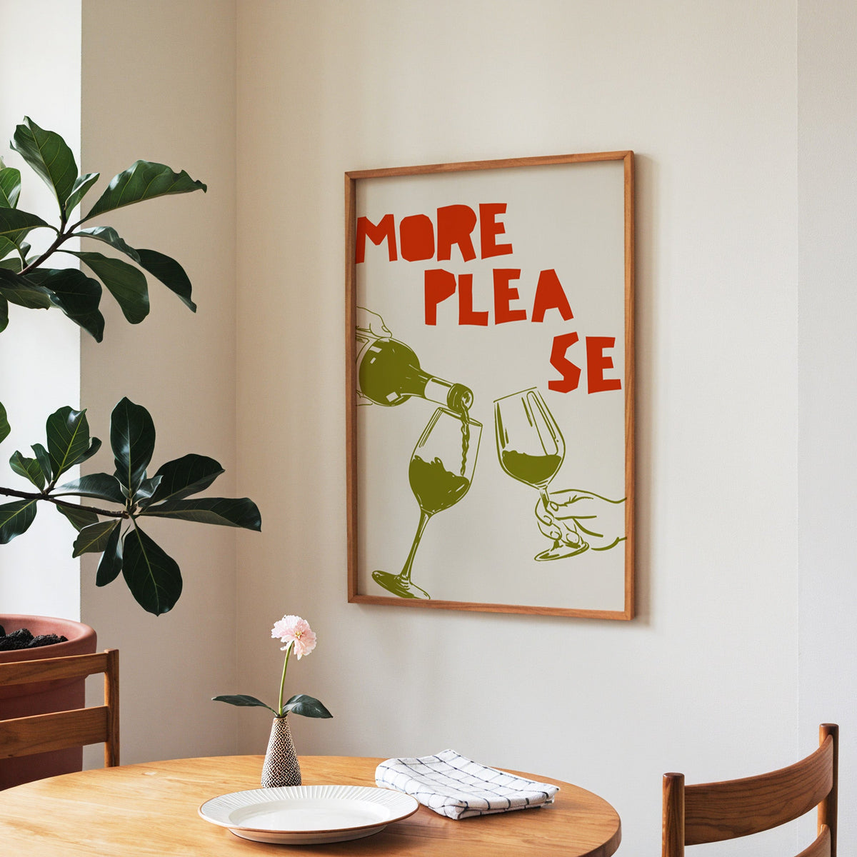 More Please wine pour print in a walnut frame above a round table beside a fiddle-leaf fig