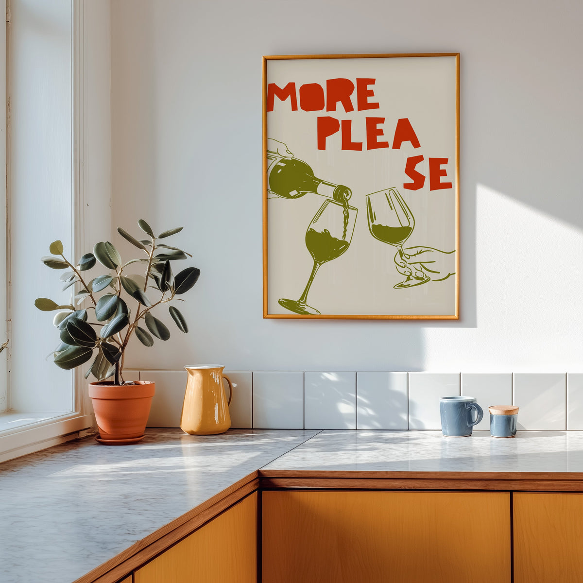 More Please wine pour print shown in a gold frame above a marble counter in a tan kitchen