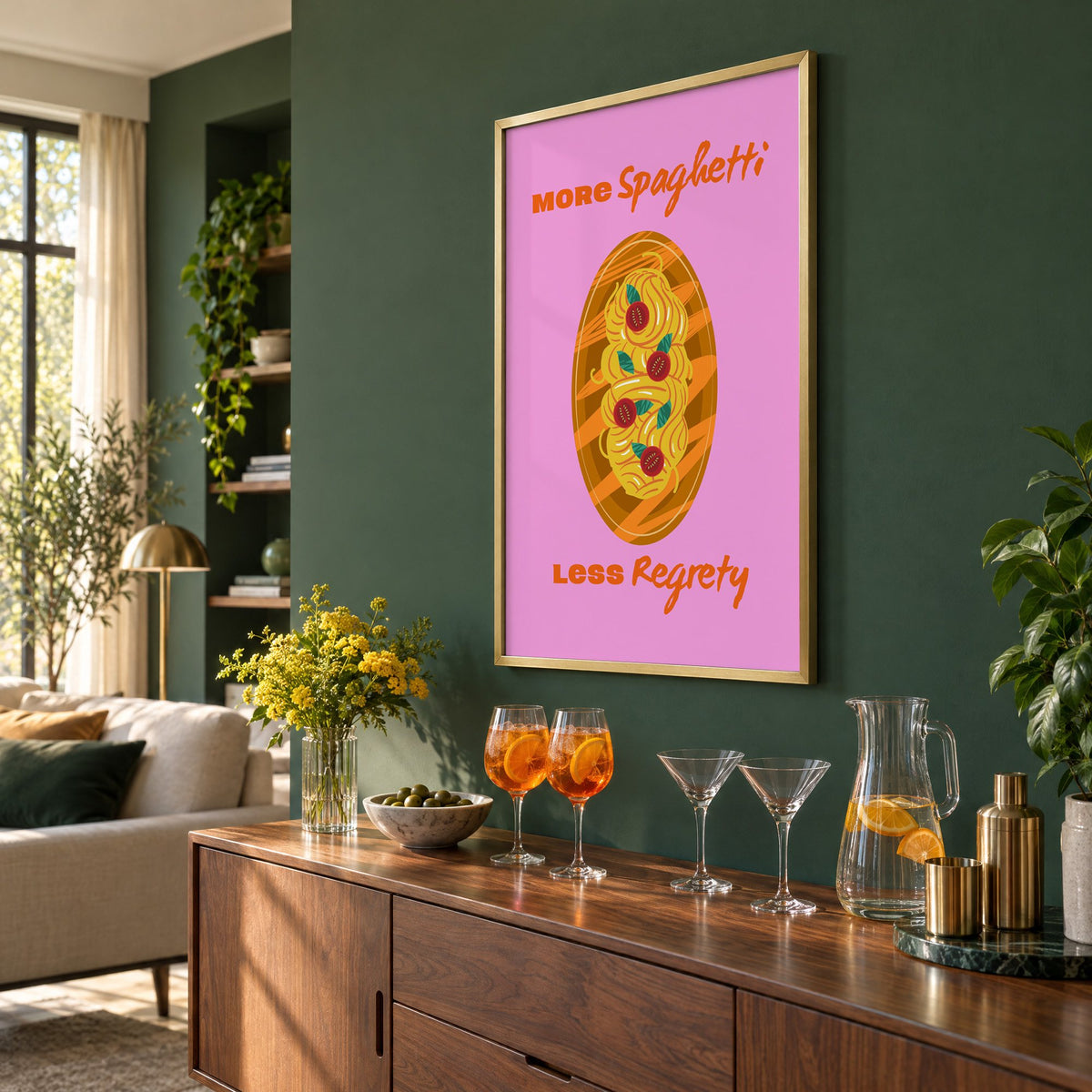 MORE Spaghetti LESS Regrety pasta plate print in a brass frame on a bottle green wall above a sideboard with spritz and martini glasses, seen at an angle