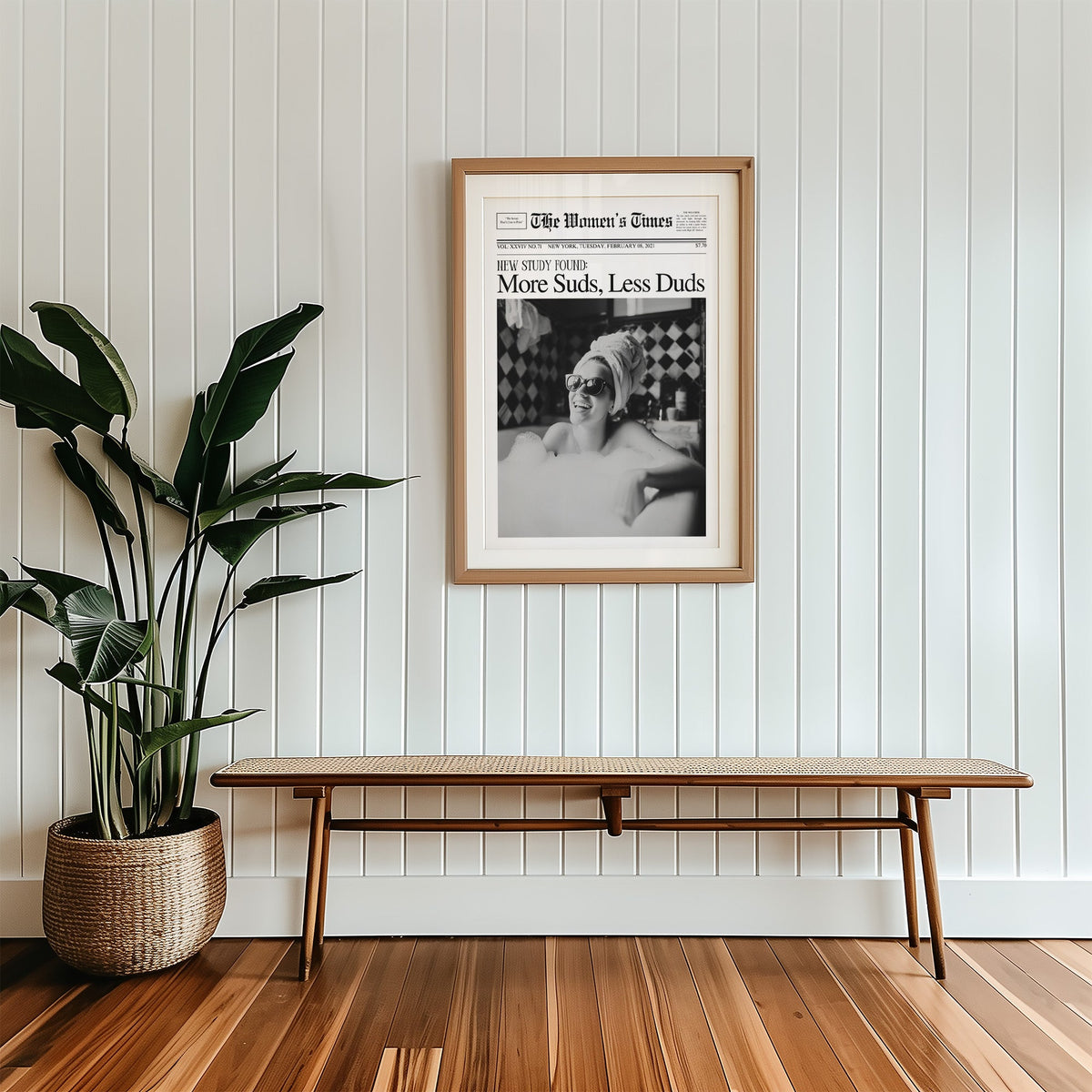Woman in bubble bath mock newspaper print in a wood frame with a white mat above a cane bench