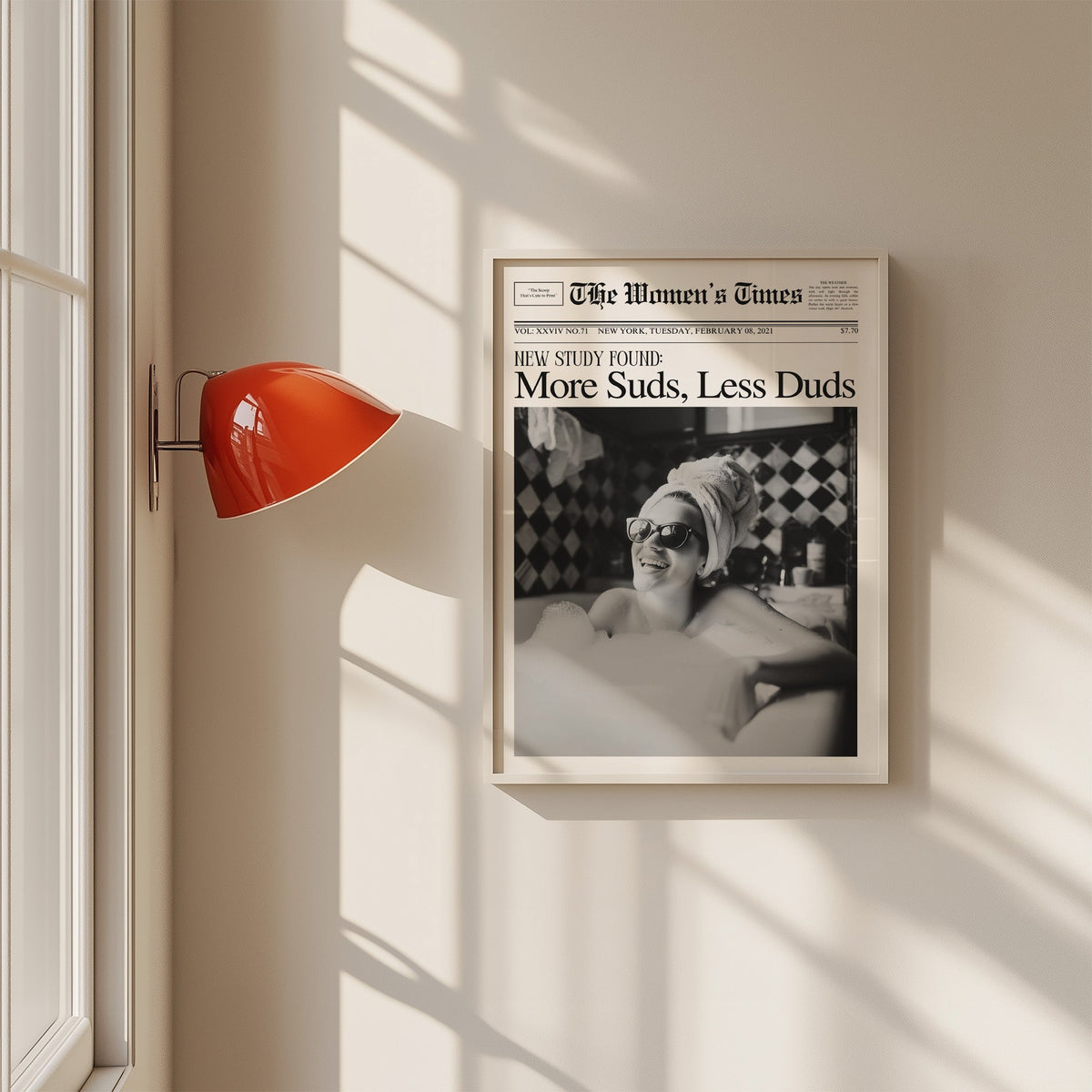 Woman in bubble bath mock newspaper print in a white frame on a sunlit wall beside a red sconce