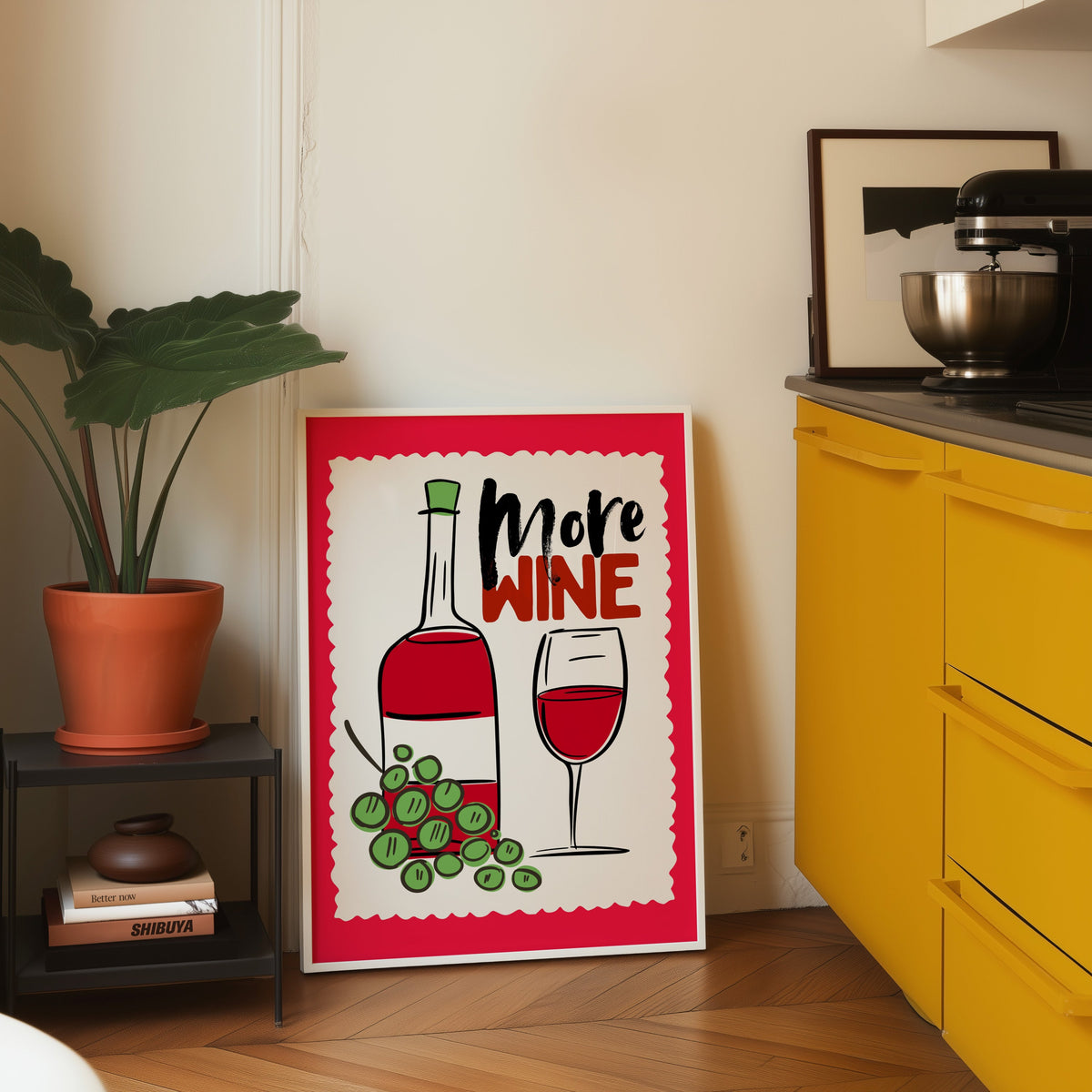 More Wine print in a white frame leaning on parquet beside a bright yellow kitchen