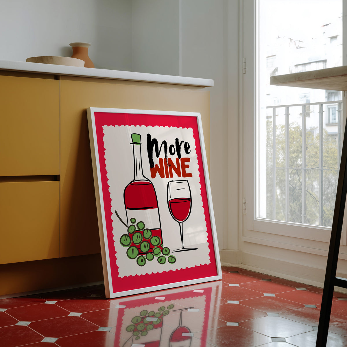 More Wine print in a white frame against yellow cabinets on a red tiled floor