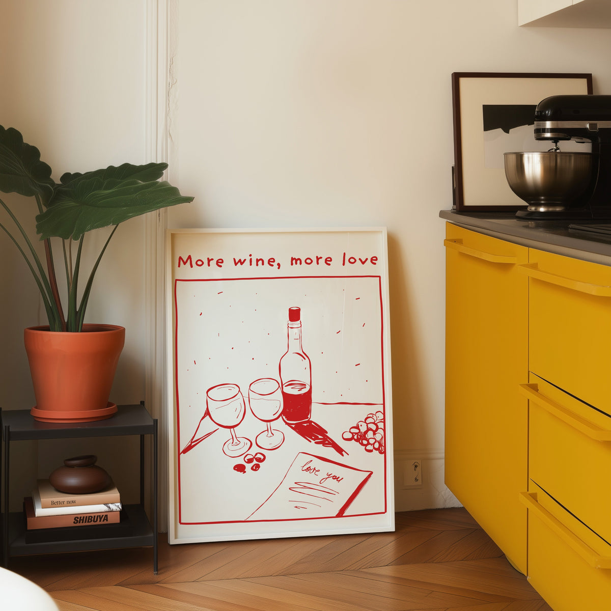More Wine More Love print in a white frame leaning on parquet beside a bright yellow kitchen