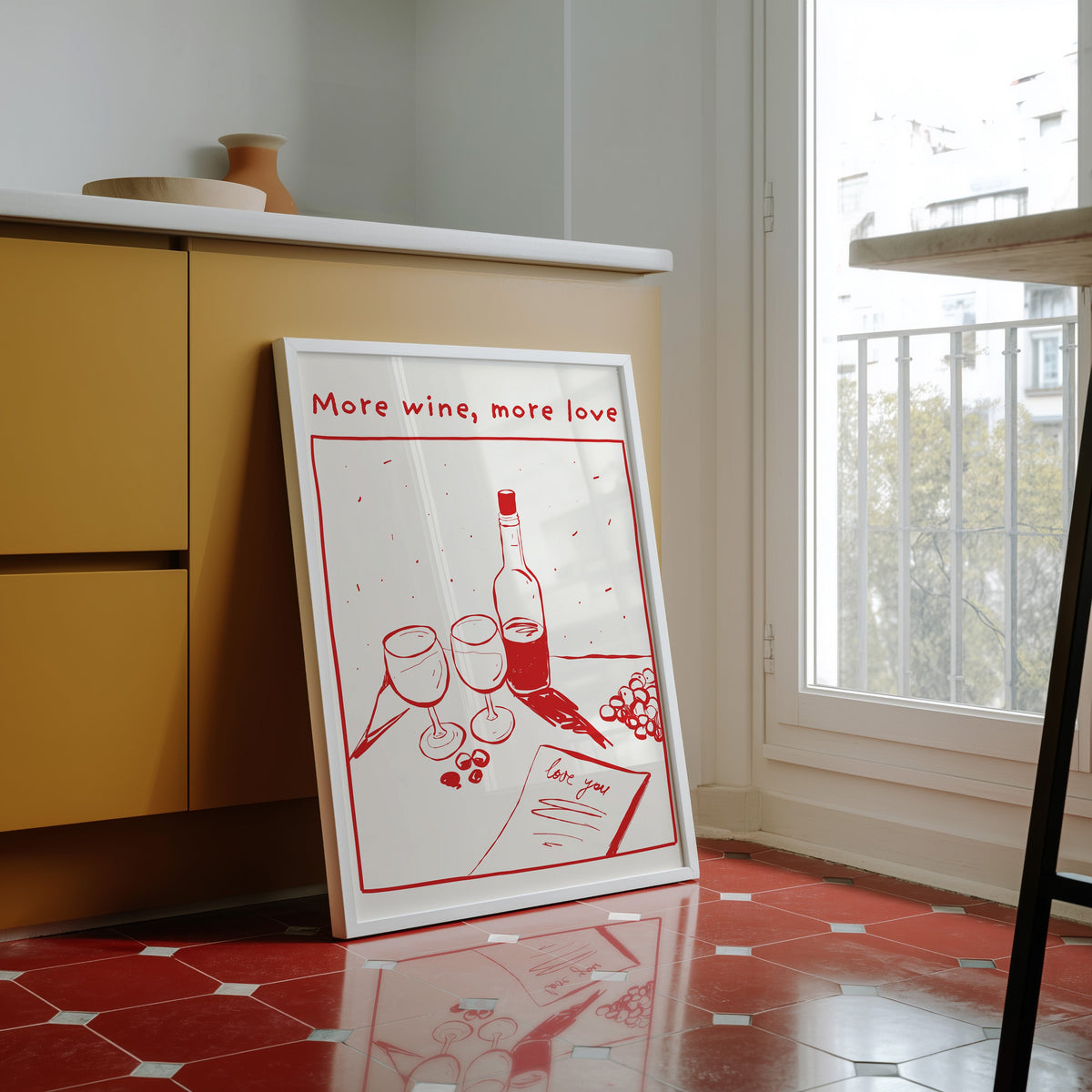 More Wine More Love print in a white frame against yellow cabinets on a red tiled floor