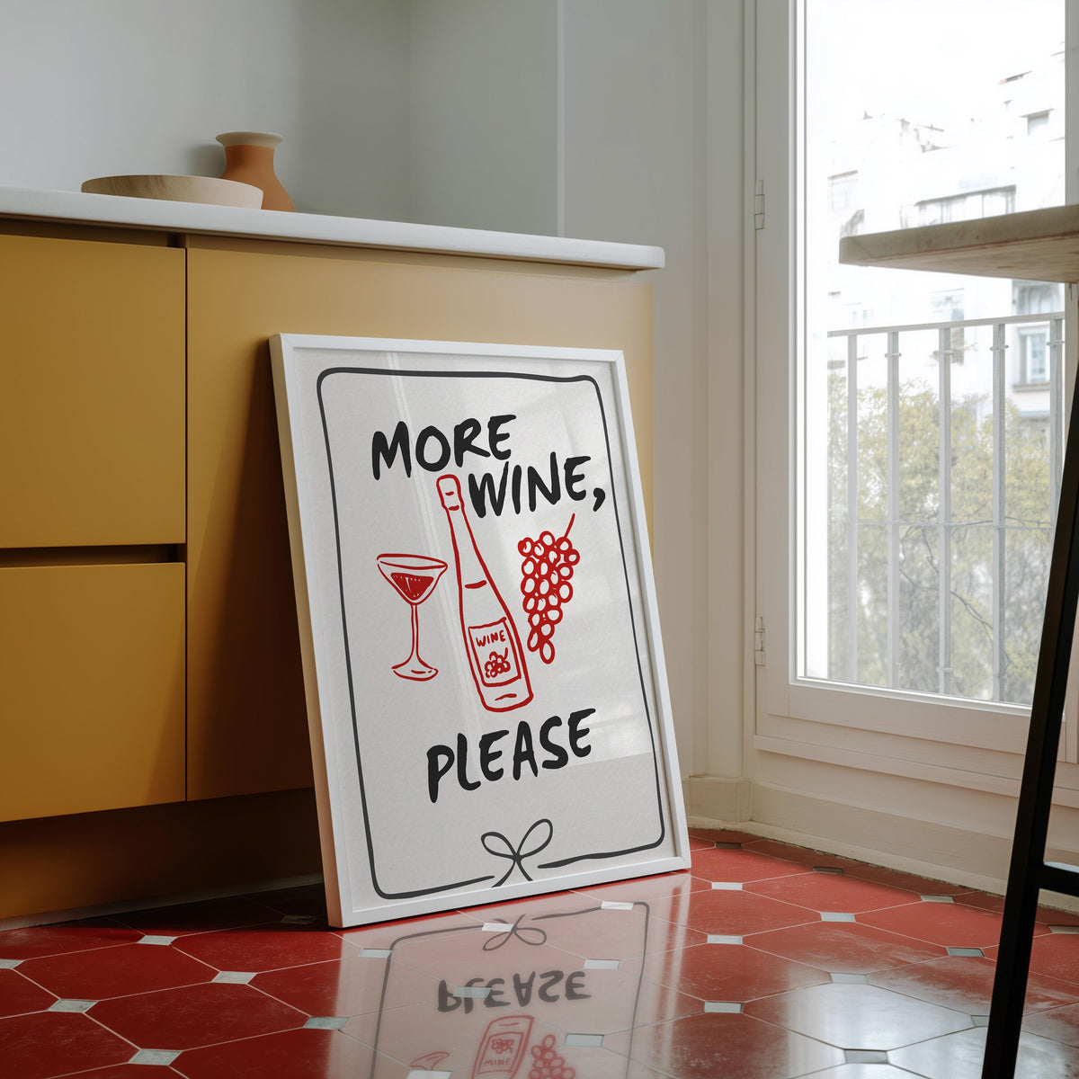 More Wine Please print in a white frame against yellow cabinets on a red tiled floor