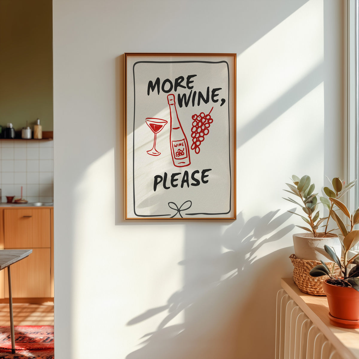 More Wine Please print shown in a gold frame in sunlight with plants and a kitchen beyond