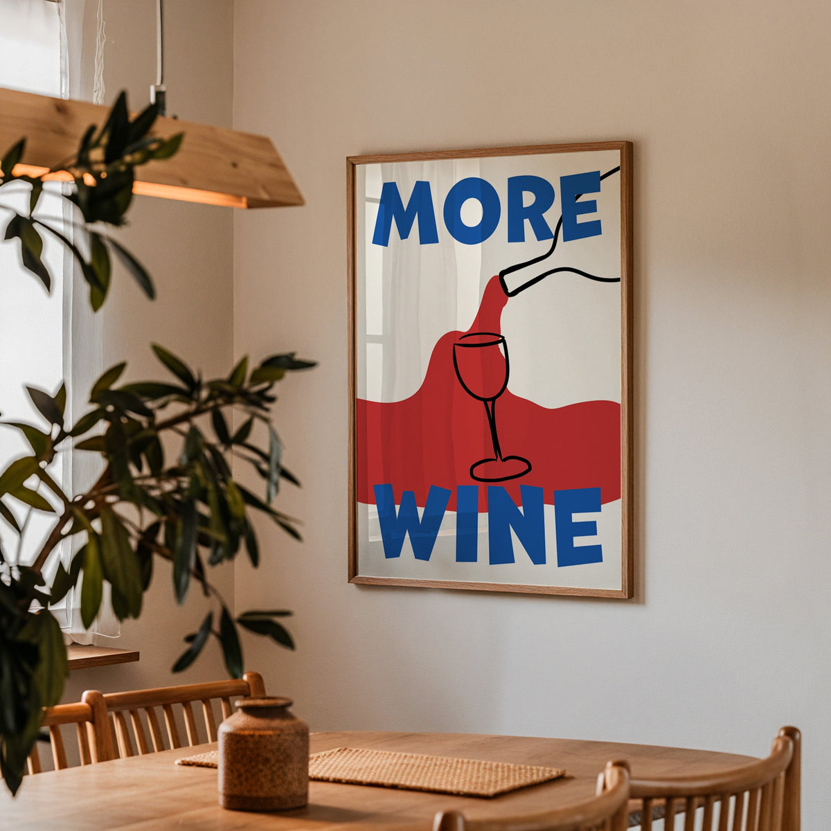 More wine red pour print in a walnut frame above a dining table beside an olive tree