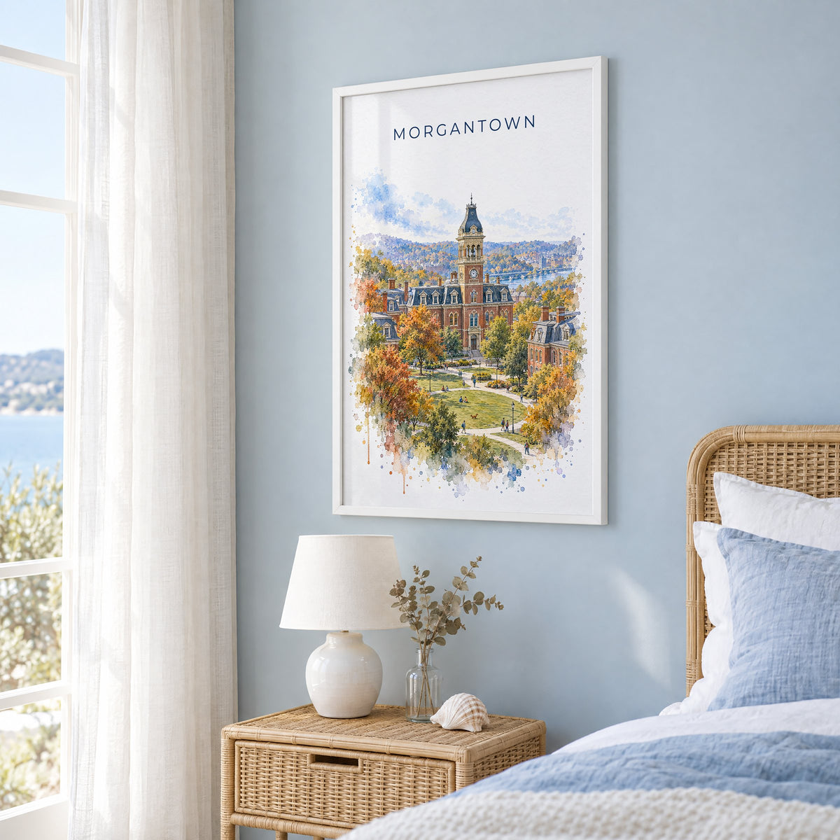 Morgantown watercolor print in a white frame on a pale blue wall beside a rattan bed in a coastal bedroom