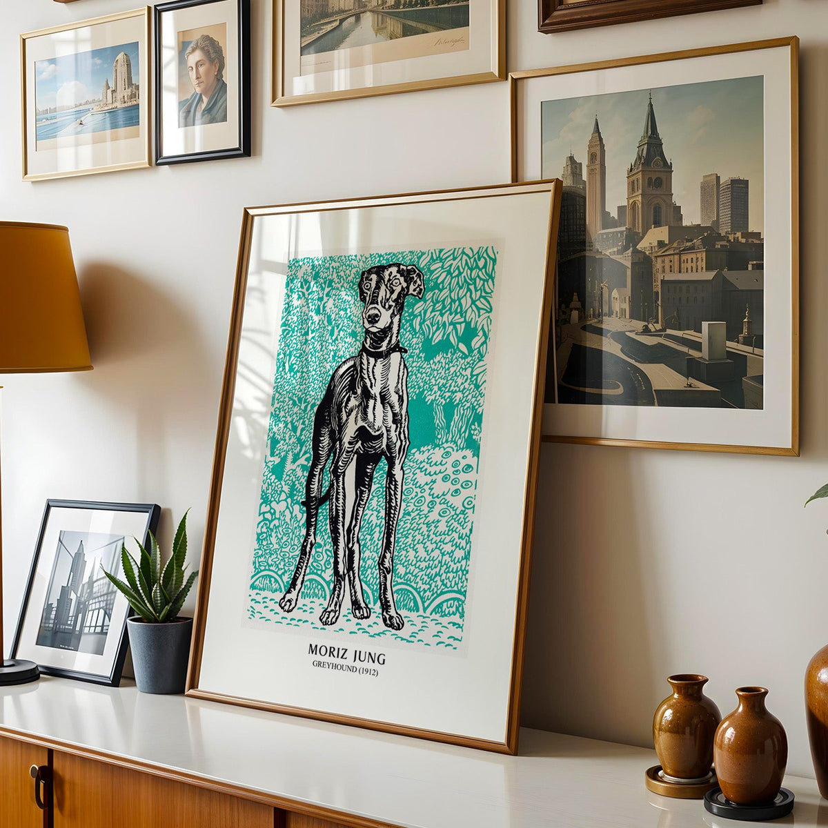 Greyhound print shown in a gold frame leaning on a sideboard in a gallery wall