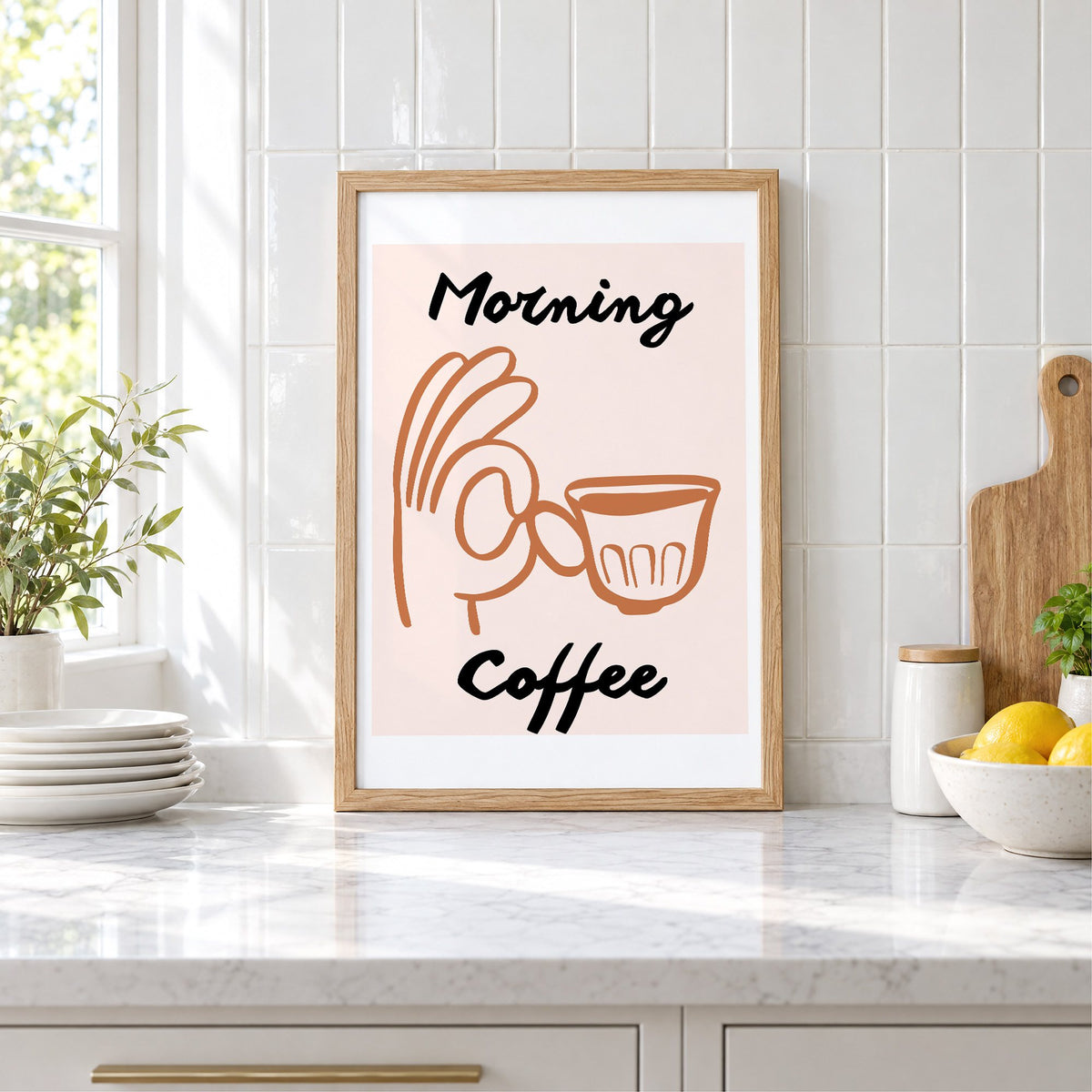 Morning Coffee terracotta hand cup print in an oak frame leaning on a marble counter by white tiles and lemons