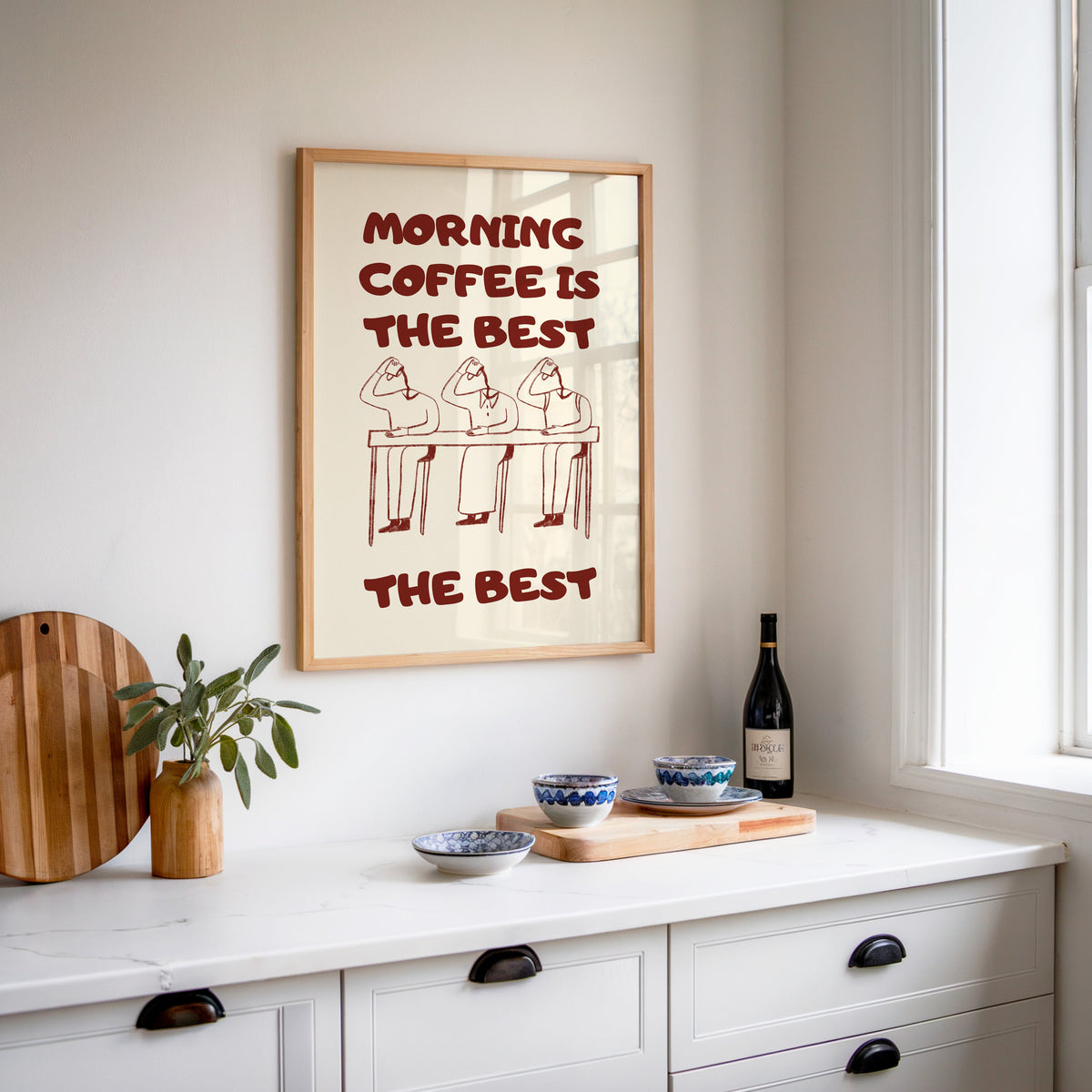 Morning Coffee Is The Best print in an oak frame above a white sideboard with a bottle of wine