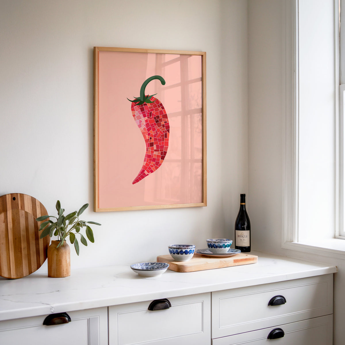 Mosaic chilli print in an oak frame above a white sideboard with a bottle of wine