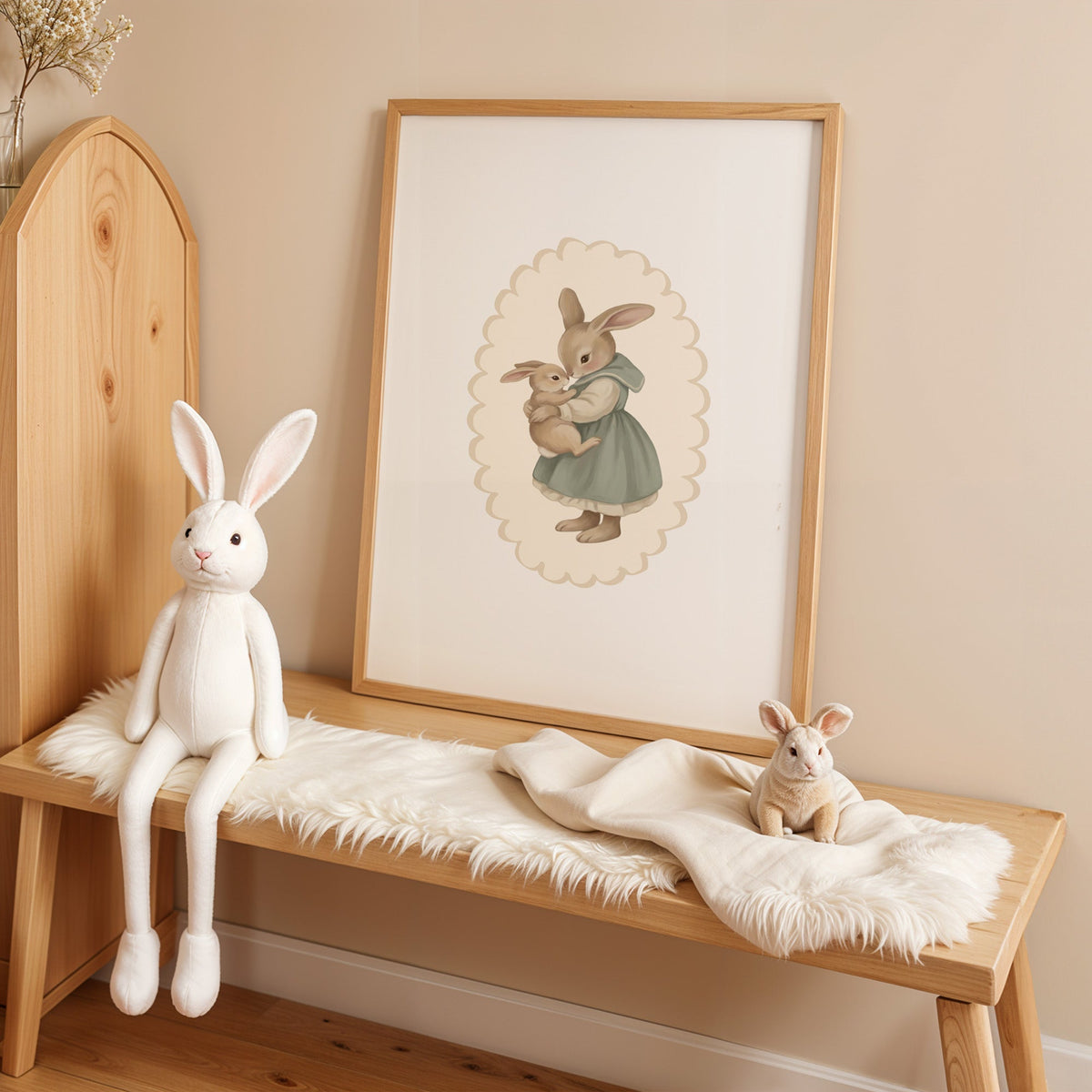 Mother rabbit in sage dress hugging baby bunny nursery print in an oak frame on a sheepskin bench beside a white plush bunny