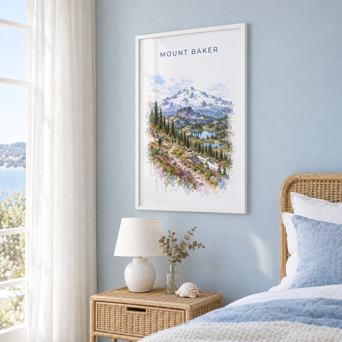 Mount Baker watercolor print in a white frame on a pale blue wall beside a rattan bed in a coastal bedroom
