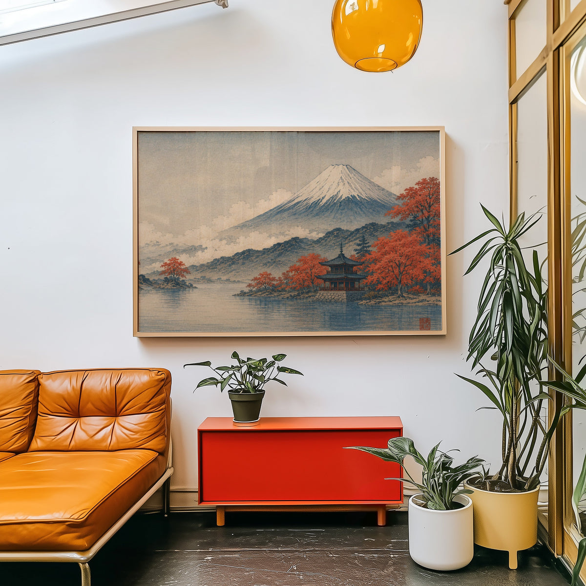 Mount Fuji autumn lake and pagoda print in a light wood frame above a red cabinet beside a tan leather daybed