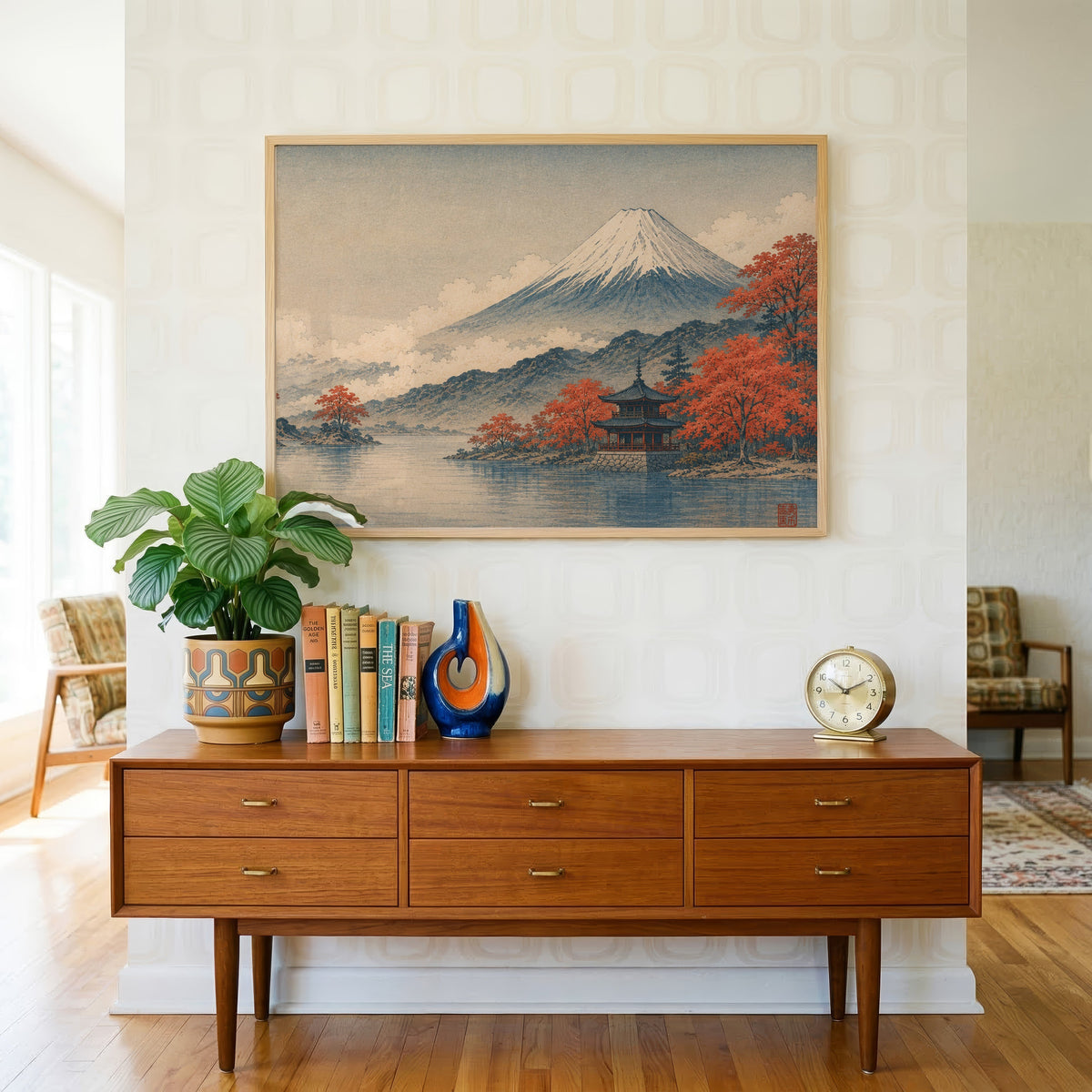 Mount Fuji autumn lake and pagoda print in a light oak frame above a teak credenza with books and a brass clock