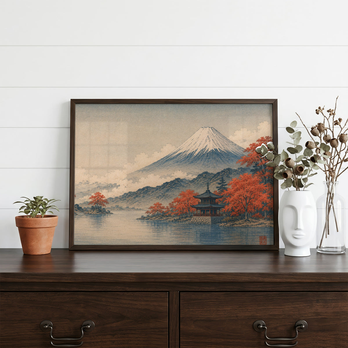 Mount Fuji autumn lake and pagoda print in a dark walnut frame on a dark wood dresser beside a white face vase