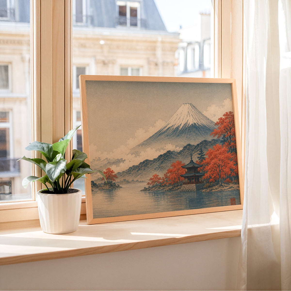 Mount Fuji autumn lake and pagoda print in a light wood frame leaning on a sunny windowsill by sheer curtains