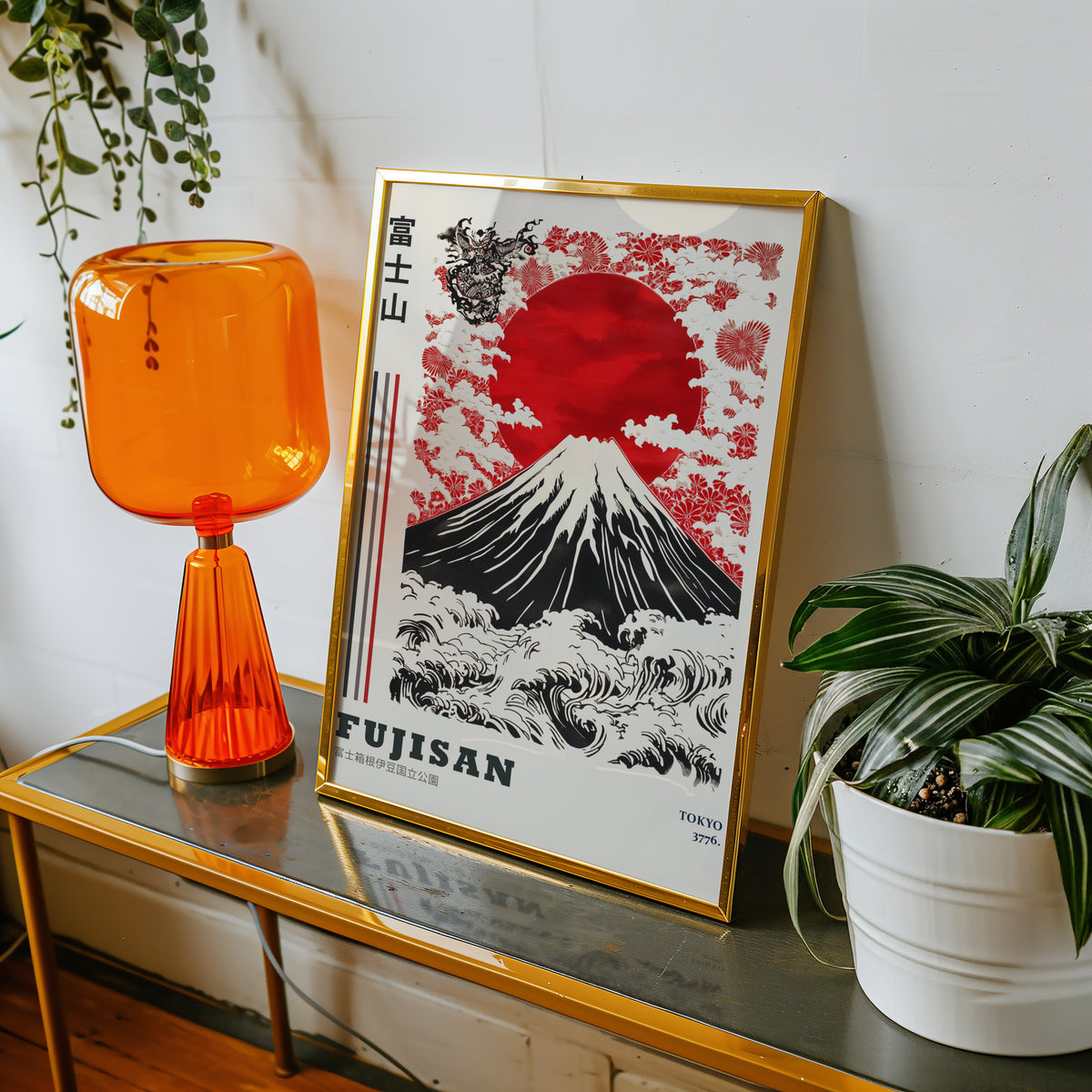 Red sun Mount Fuji floral wave print shown in a gold frame on a console beside an orange glass lamp