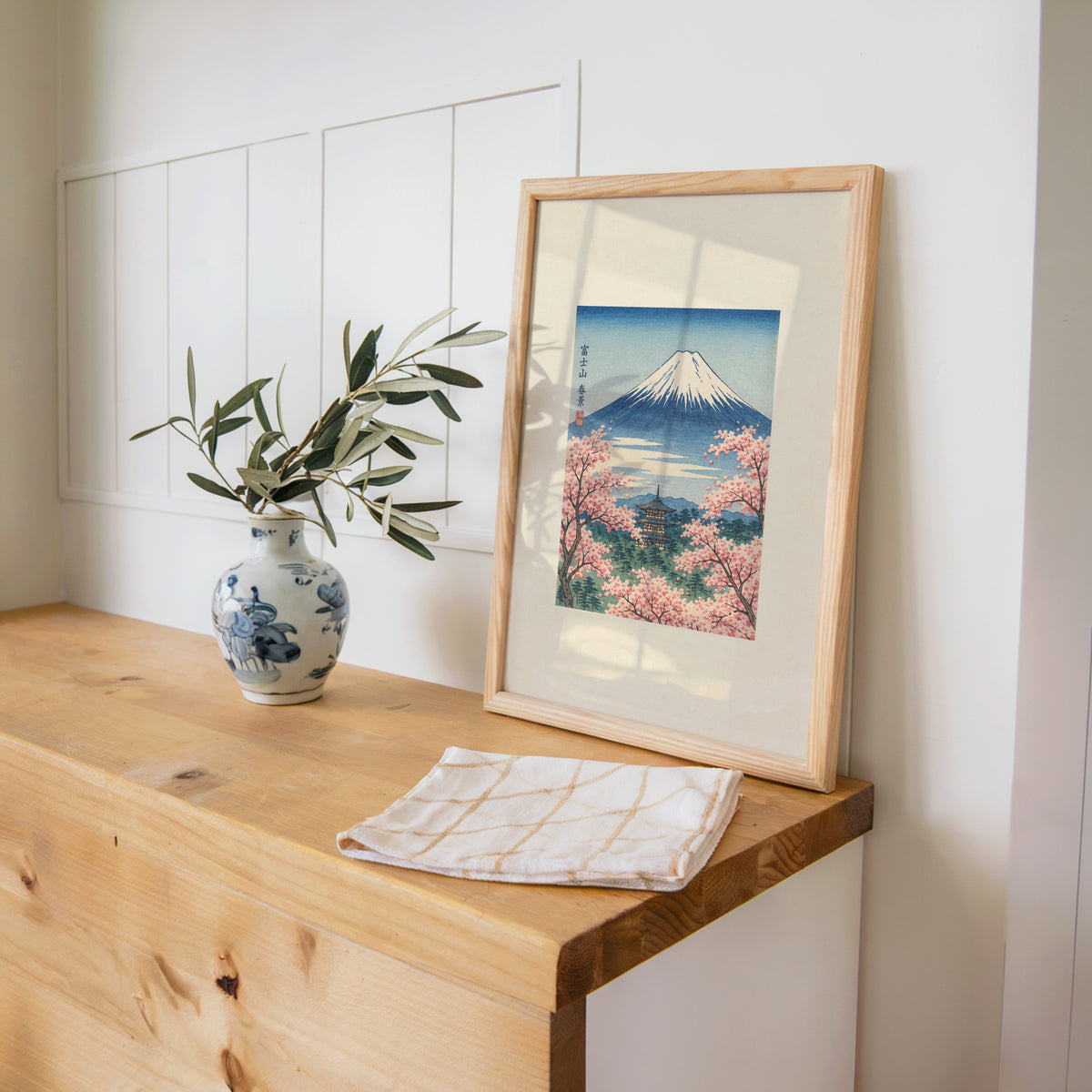 Mount Fuji with pagoda in spring print in a pine frame on a wooden counter beside a blue and white porcelain vase