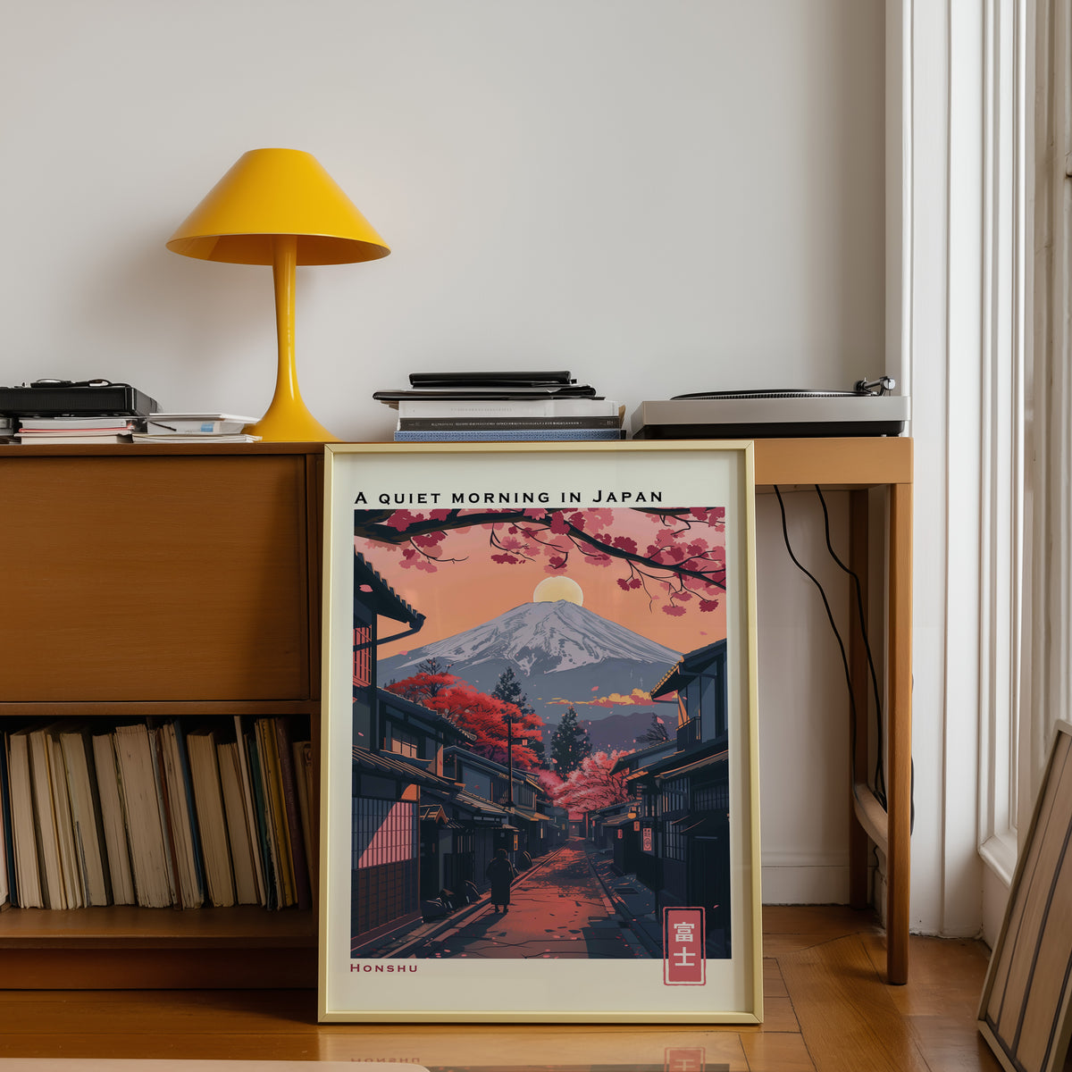 Quiet morning Fuji street print shown in a gold frame below a teak desk with a yellow lamp