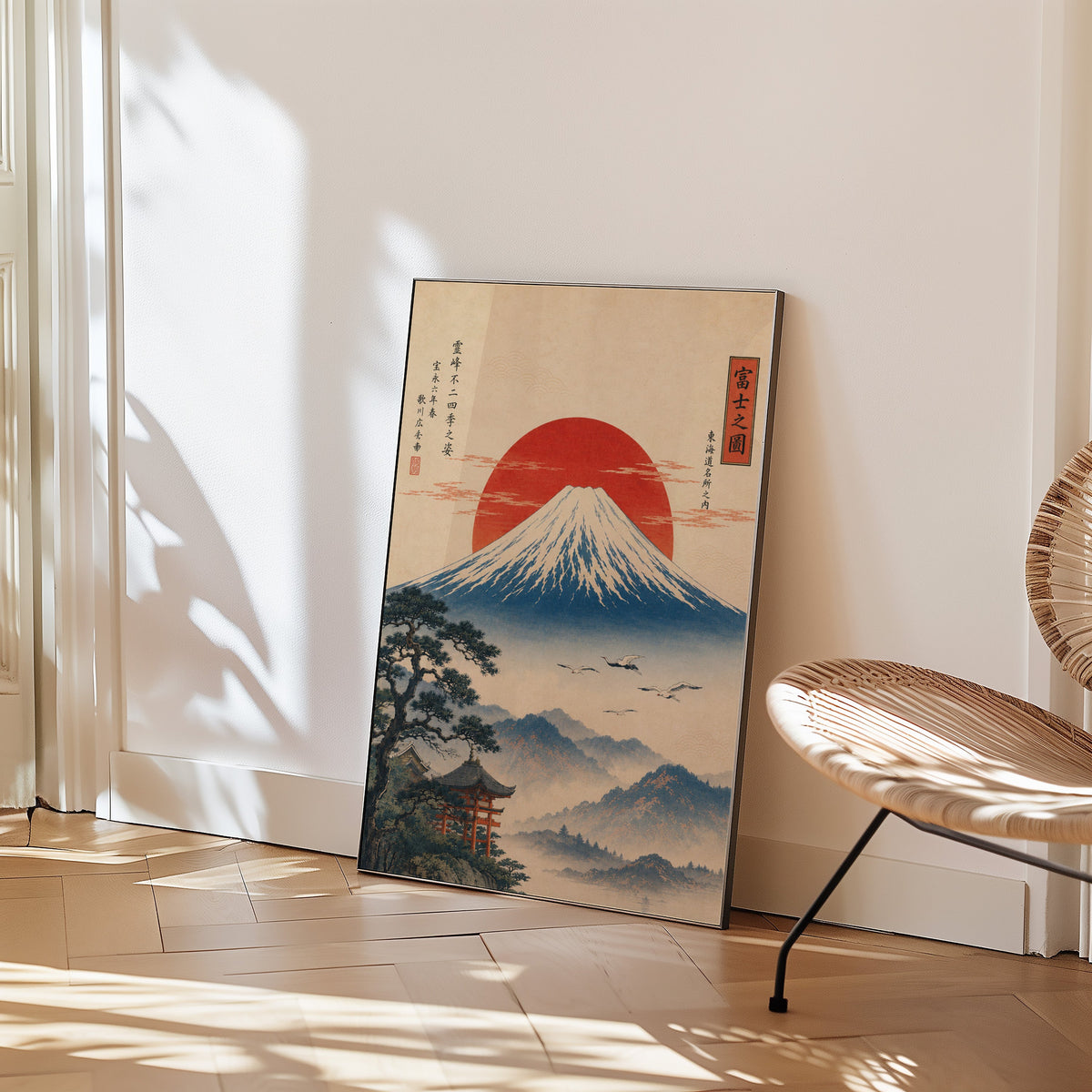 Mount Fuji with red sun and flying cranes print in a black frame leaning on a herringbone floor beside a woven rattan chair