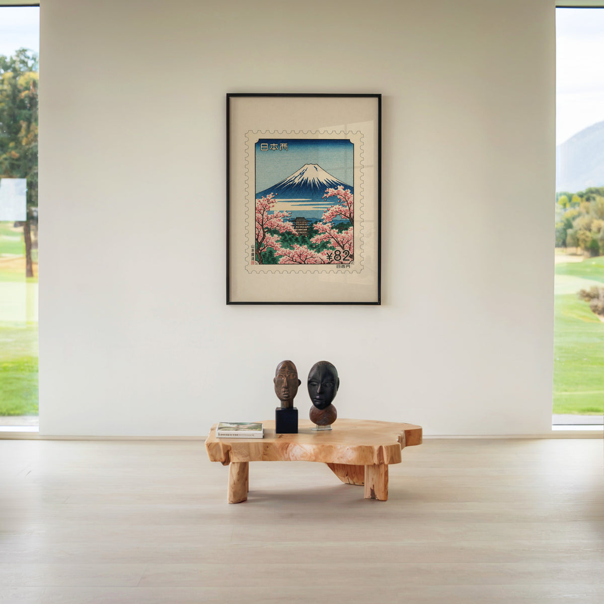 Mount Fuji sakura postage stamp print in a black frame above a live-edge wood coffee table between garden windows