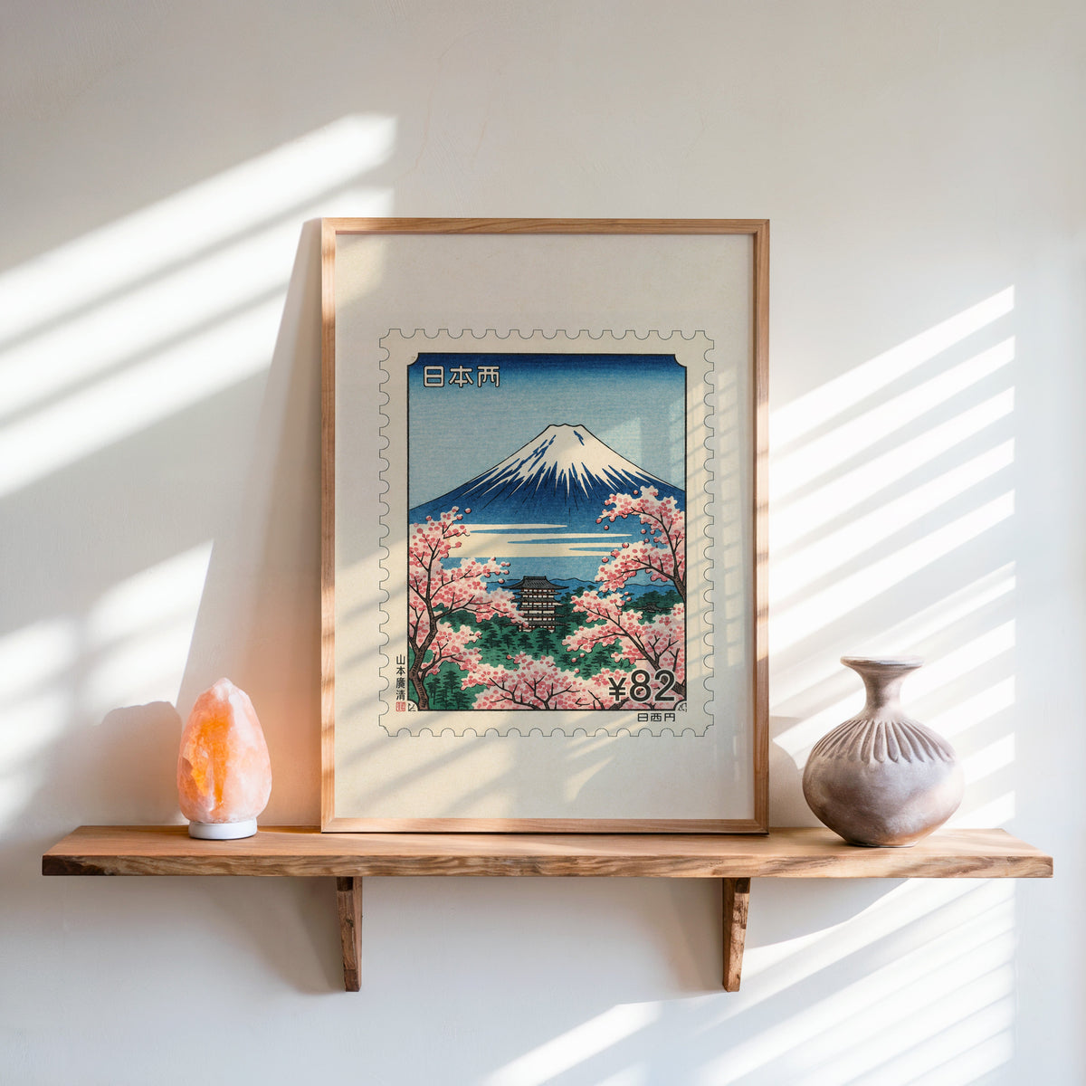Mount Fuji sakura postage stamp print in an oak frame on a live-edge wall shelf with a salt lamp and clay vase