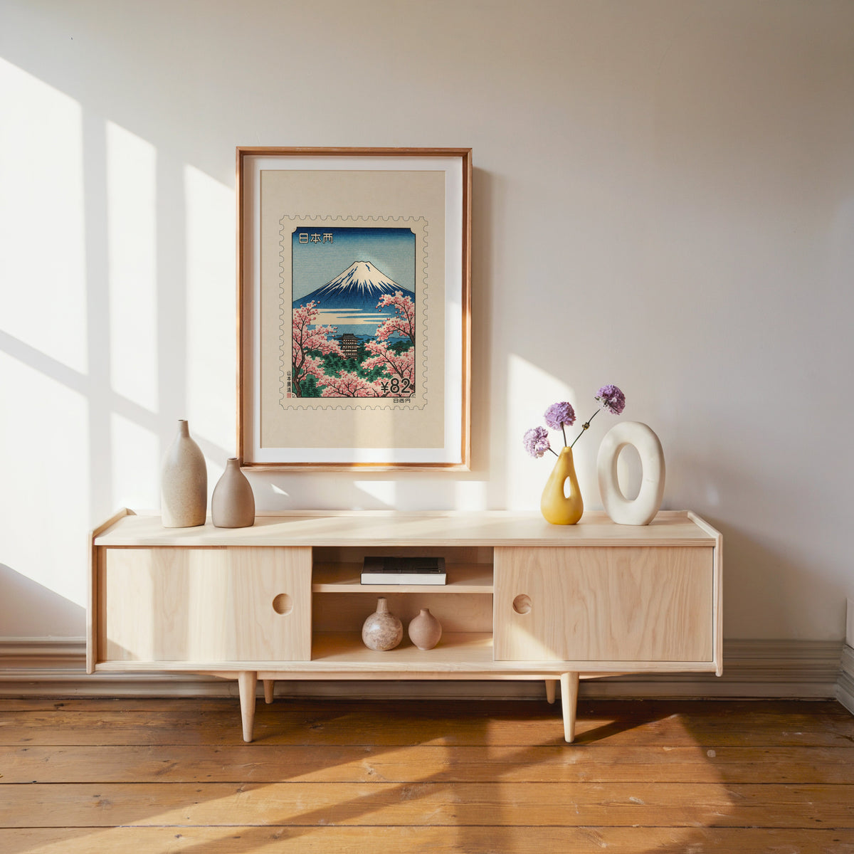 Mount Fuji sakura postage stamp print shown in a wood frame with a white mat above a pale wood media console