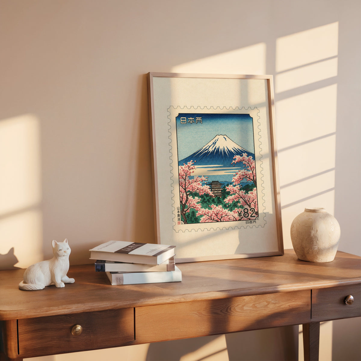 Mount Fuji sakura postage stamp print shown in a rose gold frame leaning on a wooden writing desk with books