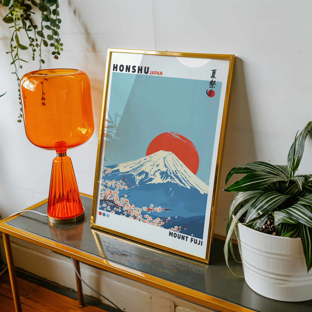 Mount Fuji red sun sakura print shown in a gold frame on a console beside an orange glass lamp