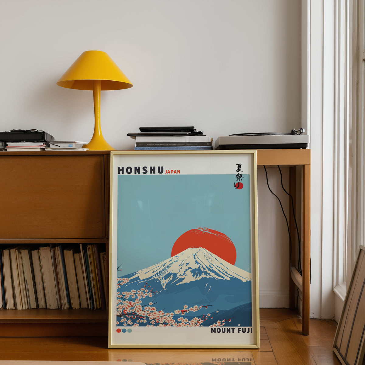 Mount Fuji red sun sakura print shown in a gold frame below a teak desk with a yellow lamp