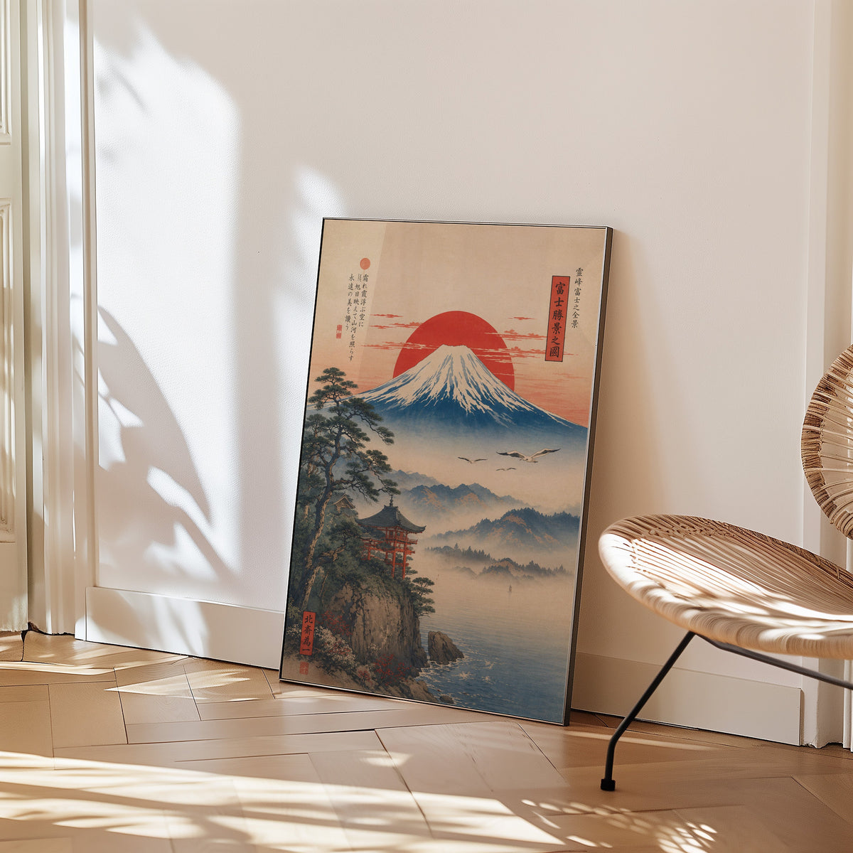 Mount Fuji sunrise with cliff shrine print in a black frame leaning on a herringbone floor beside a woven rattan chair