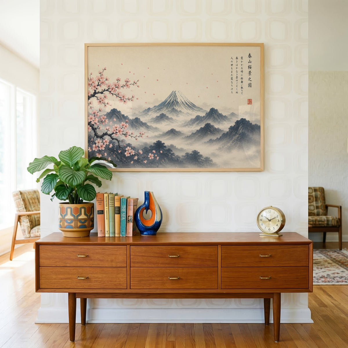 Mount Fuji and sakura ink painting print in a light oak frame above a teak credenza with books and a brass clock