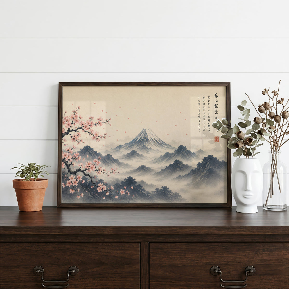 Mount Fuji and sakura ink painting print in a dark walnut frame on a dark wood dresser beside a white face vase