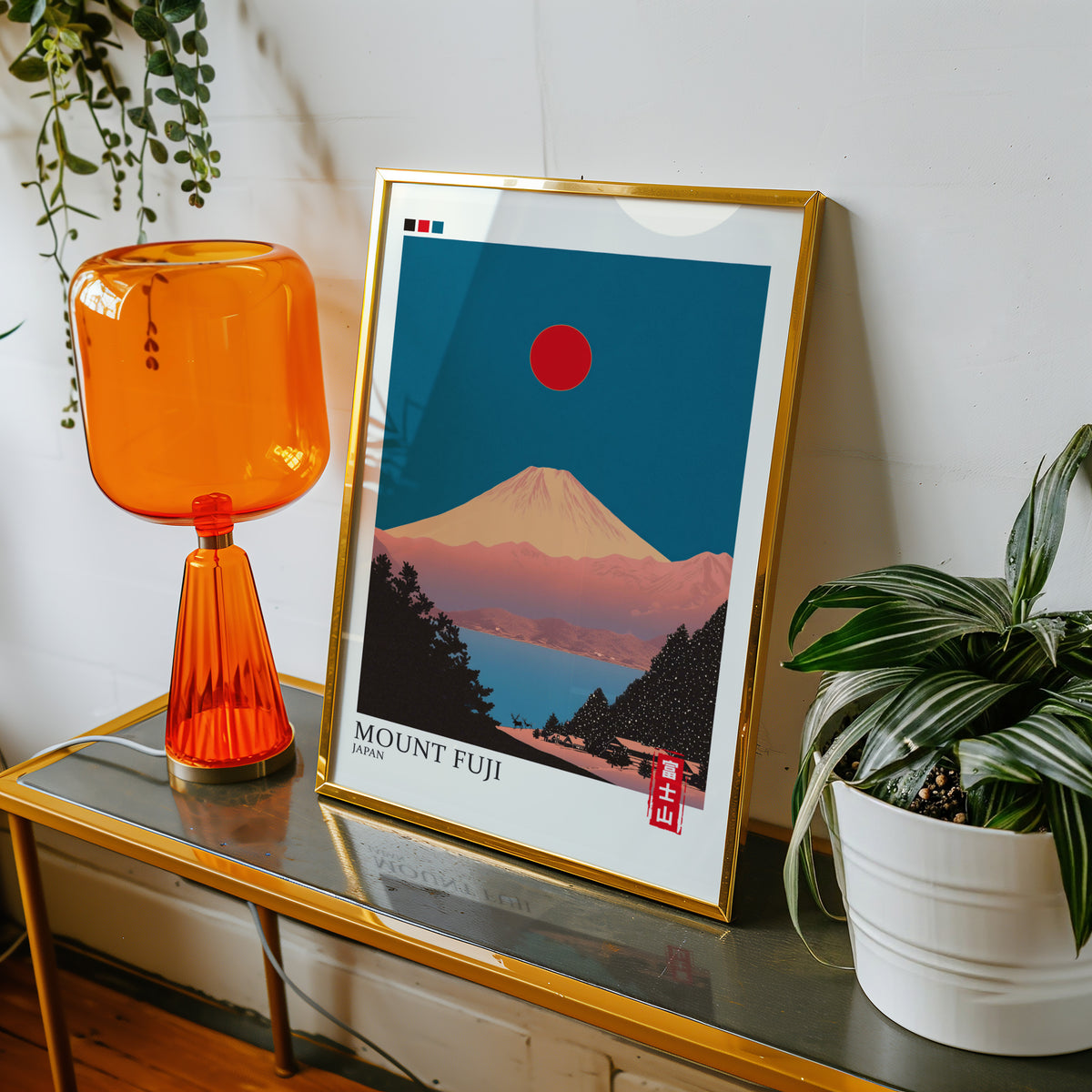 Minimalist Fuji teal sky print shown in a gold frame on a console beside an orange glass lamp