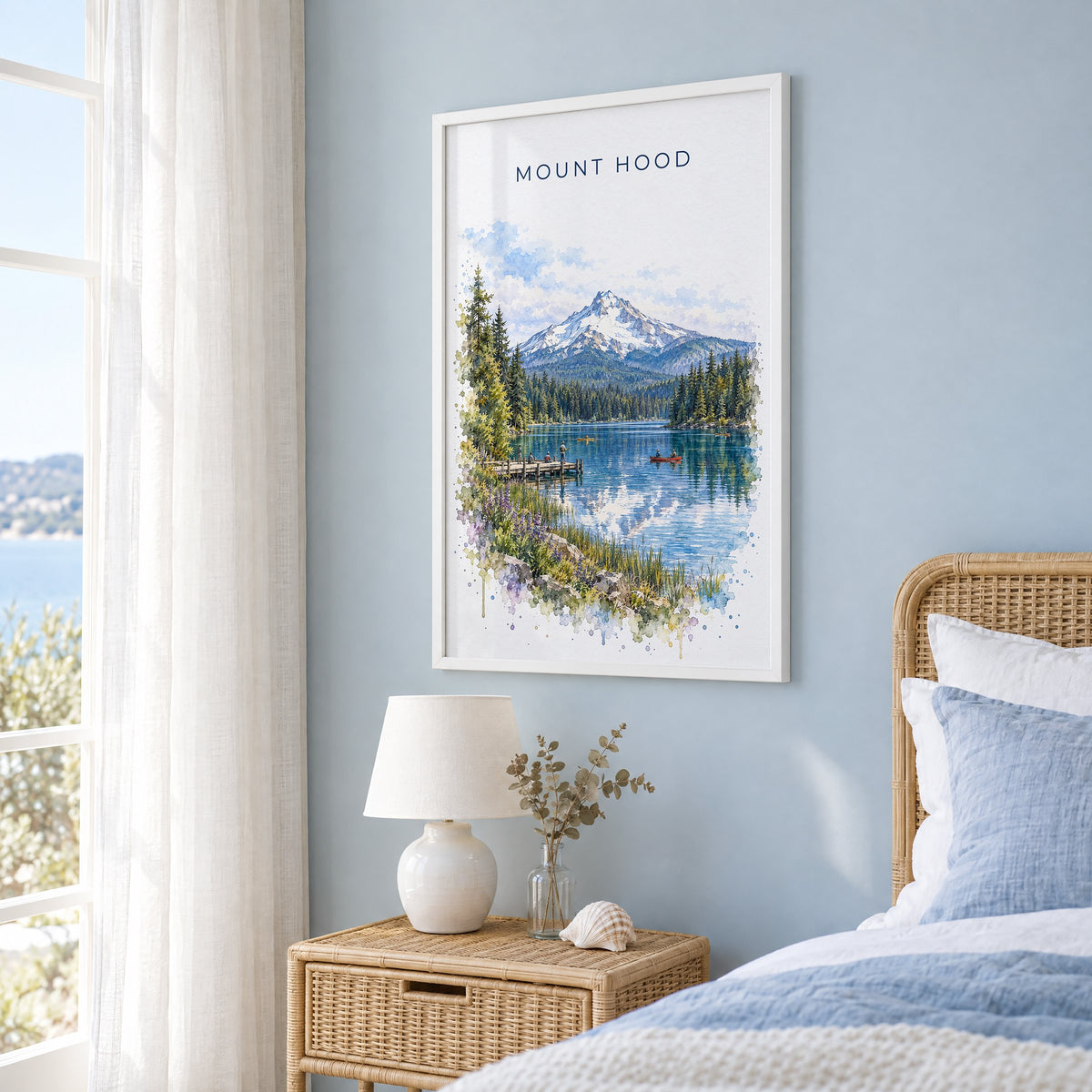 Mount Hood watercolor print in a white frame on a pale blue wall beside a rattan bed in a coastal bedroom