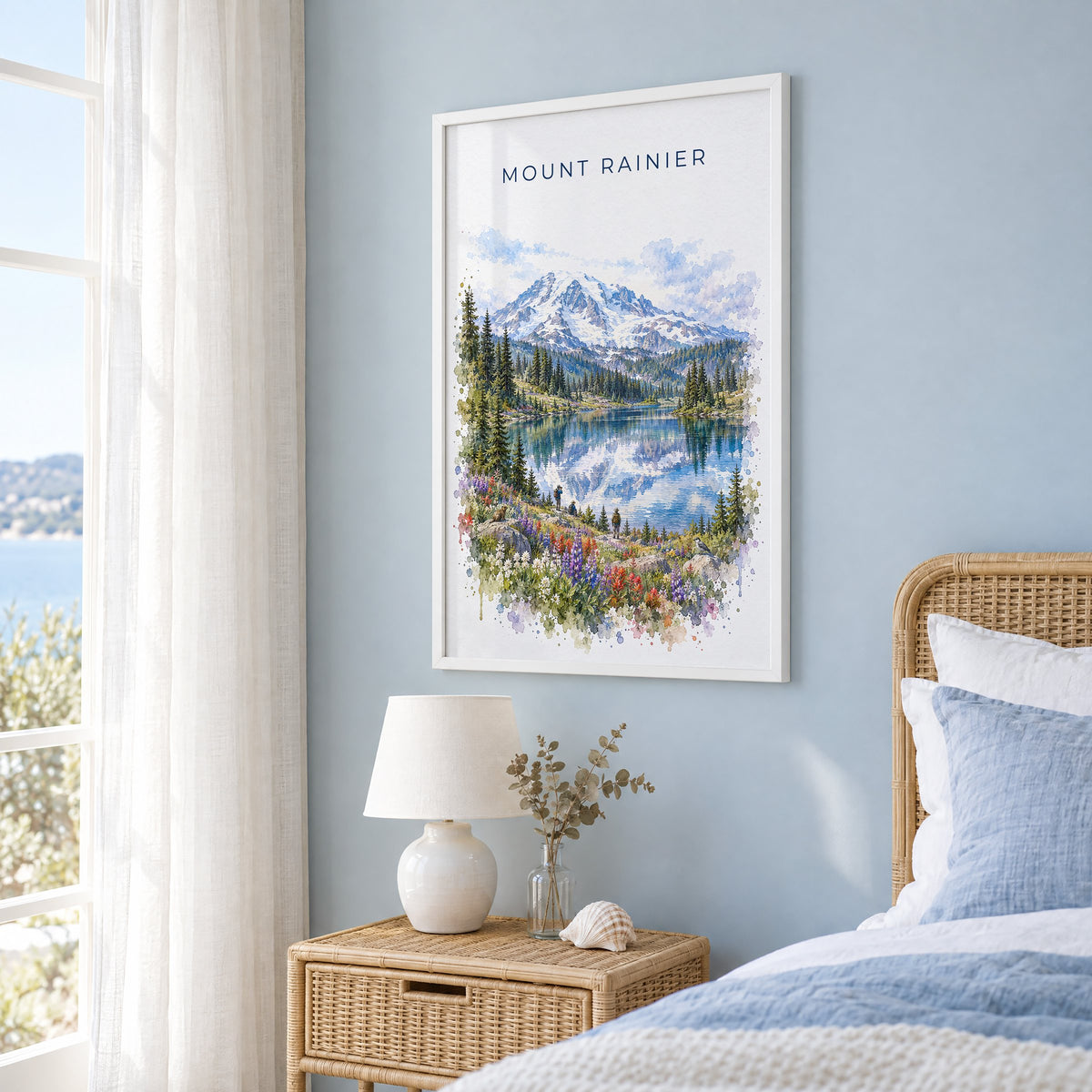 Mount Rainier National Park watercolor print in a white frame on a pale blue wall beside a rattan bed in a coastal bedroom