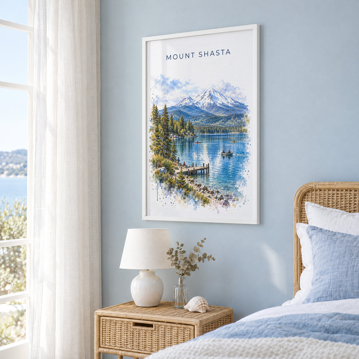 Mount Shasta watercolor print in a white frame on a pale blue wall beside a rattan bed in a coastal bedroom
