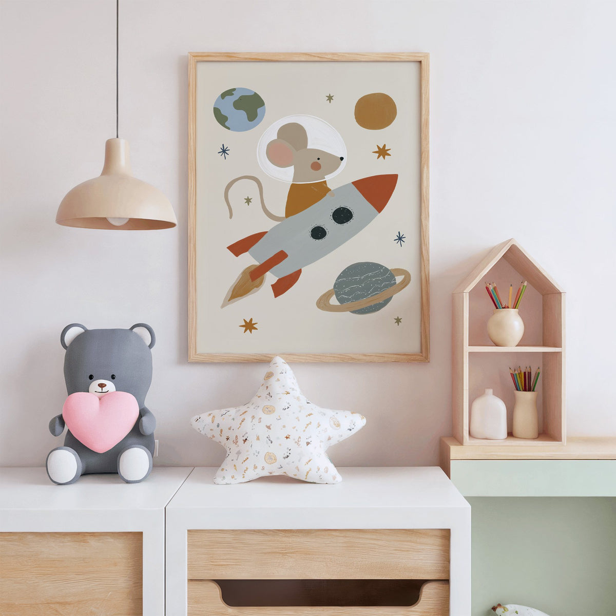 Mouse astronaut riding rocket nursery print in an oak frame above a white dresser with a star pillow and house shelf