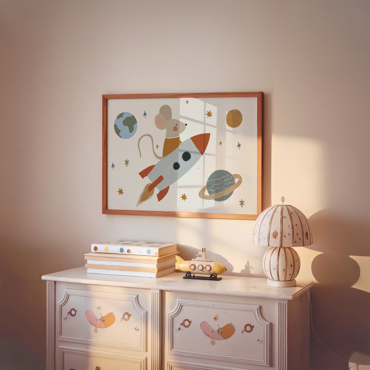 Landscape mouse astronaut riding rocket nursery print in a cherry wood frame above a painted dresser and lamp