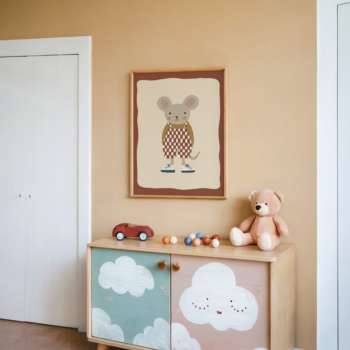 Mouse checkered overalls nursery print in an oak frame on a peach wall above a cloud-painted cabinet