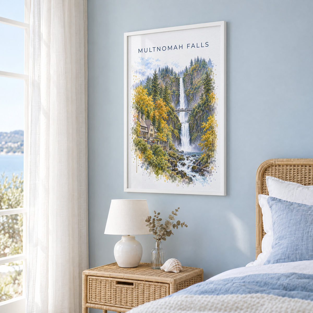 Multnomah Falls watercolor print in a white frame on a pale blue wall beside a rattan bed in a coastal bedroom