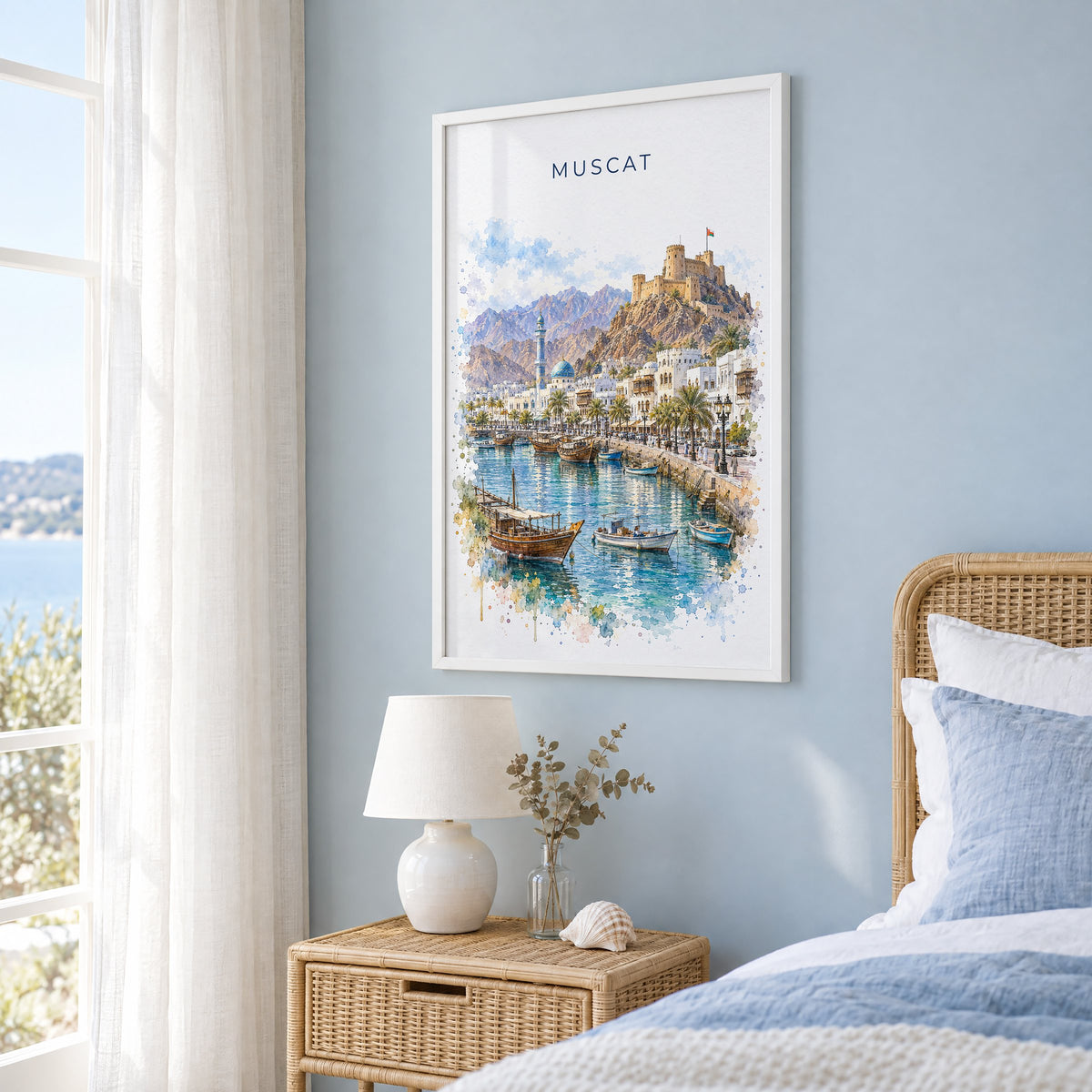 Muscat watercolor print in a white frame on a pale blue wall beside a rattan bed in a coastal bedroom