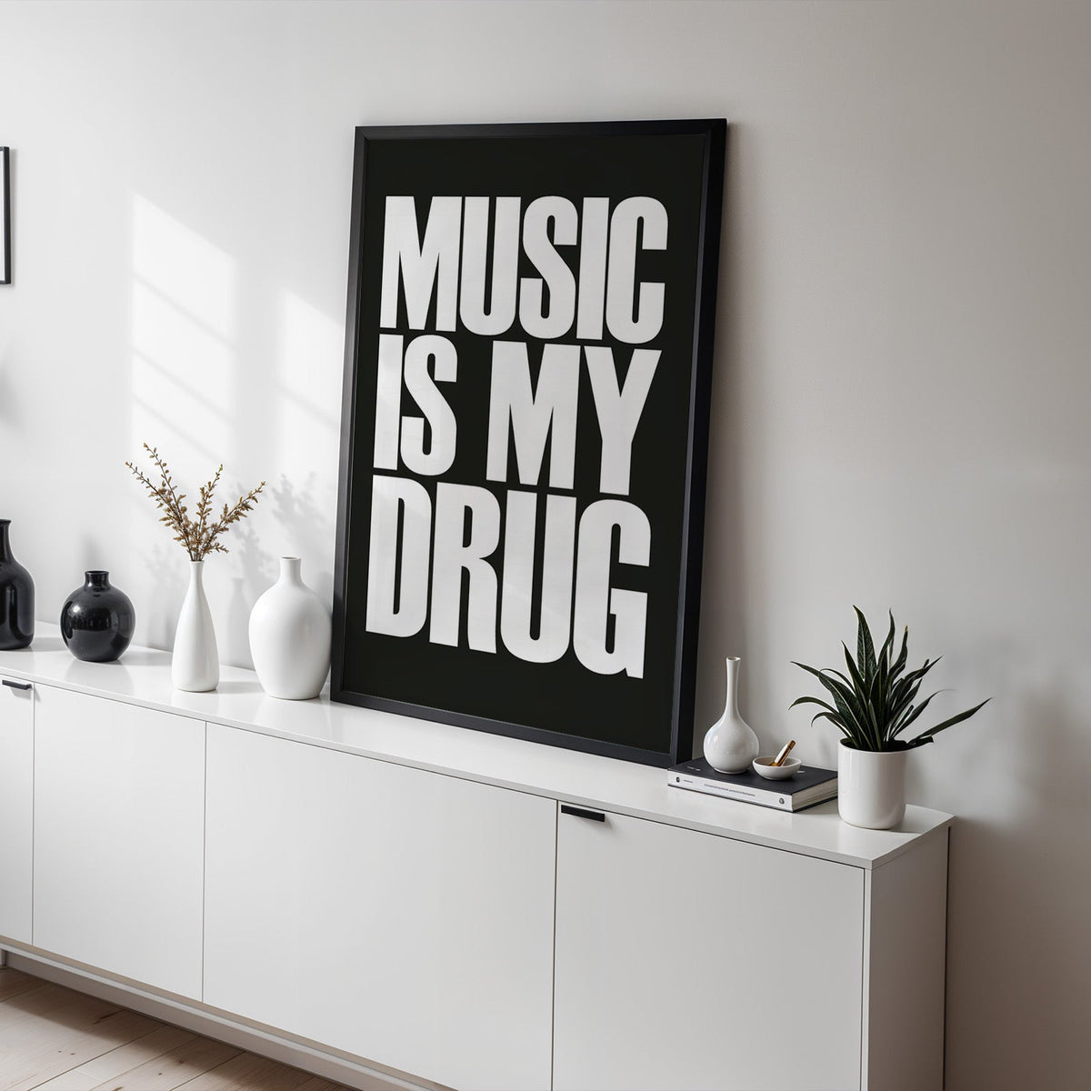 Music Is My Drug white lettering on black print in a black frame on a white sideboard with black and white vases