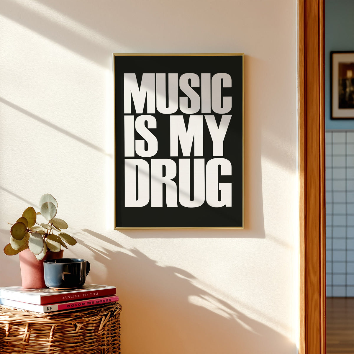 Music Is My Drug white lettering on black print shown in a gold frame above a wicker basket and stacked books